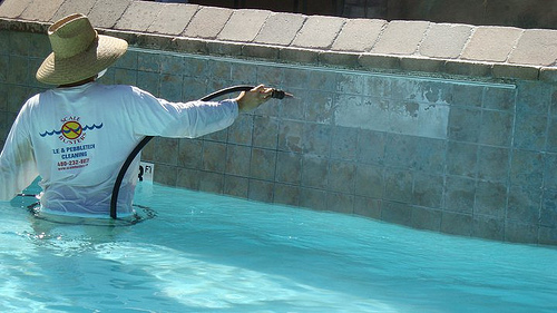 A Man Wearing A Hat Cleaning A Pool